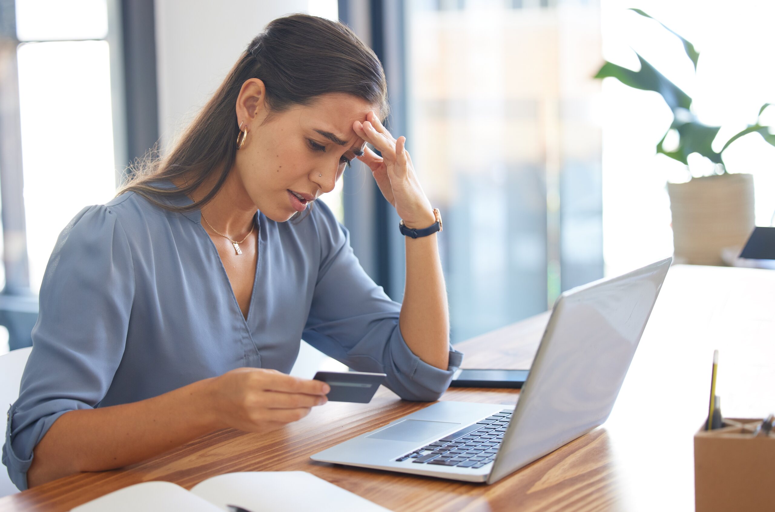 Stressed woman holding a card at her laptop asking do you have a case against your broker or financial advisor.